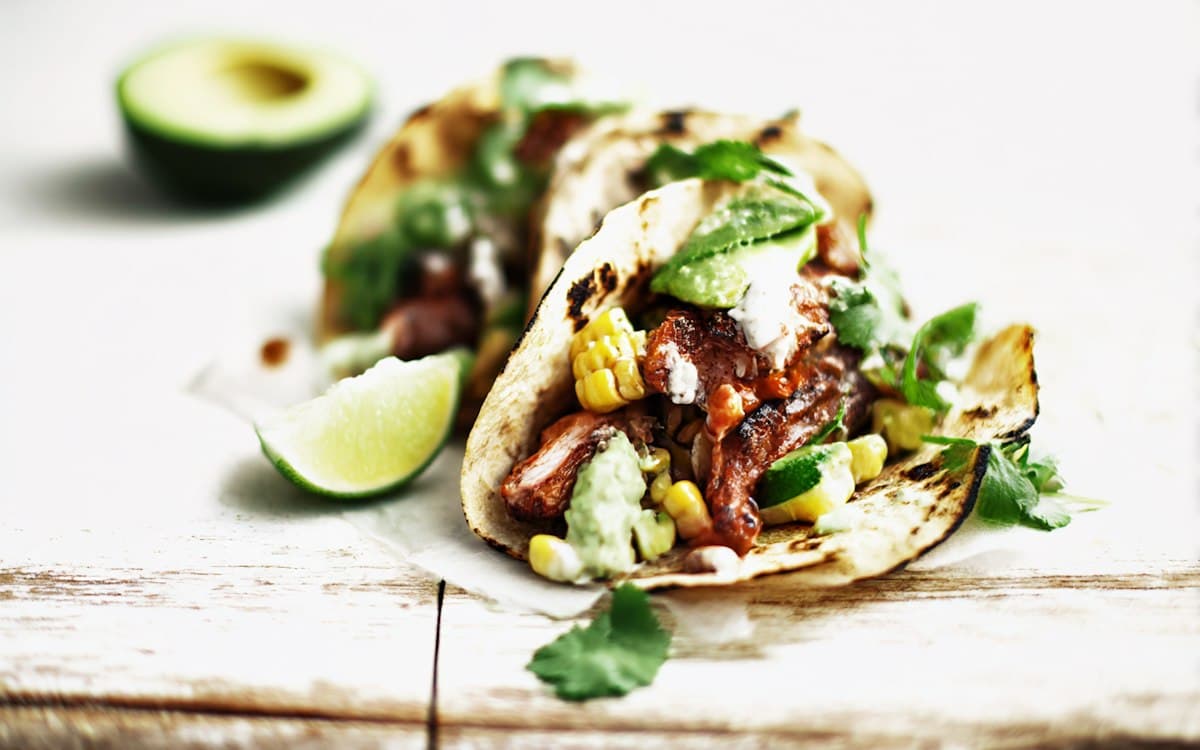 Tacos with grilled meat, avocado and lime on a rustic wooden table